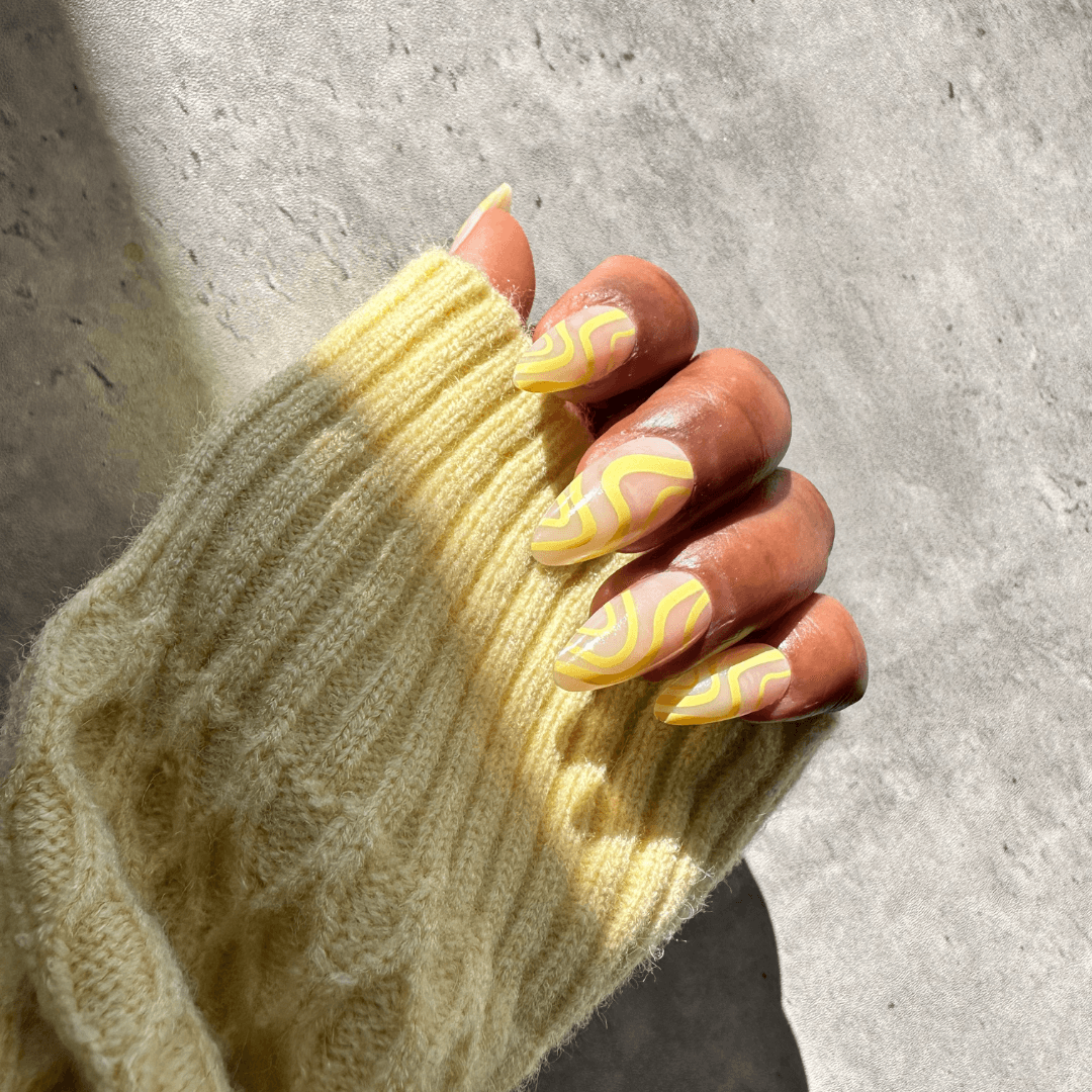 Yellow almond press-on nails with swirl design on hand