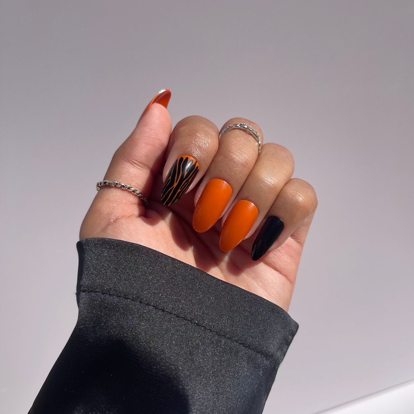 Hand with Halloween press-on nails in orange, black, and zebra pattern