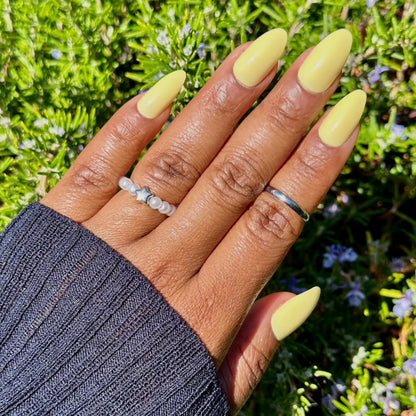 Stylish pastel yellow nails in a garden setting