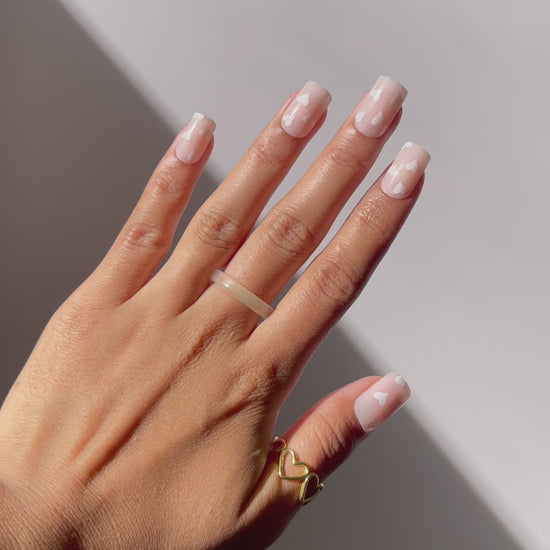 Short nude press-on nails featuring white hearts.