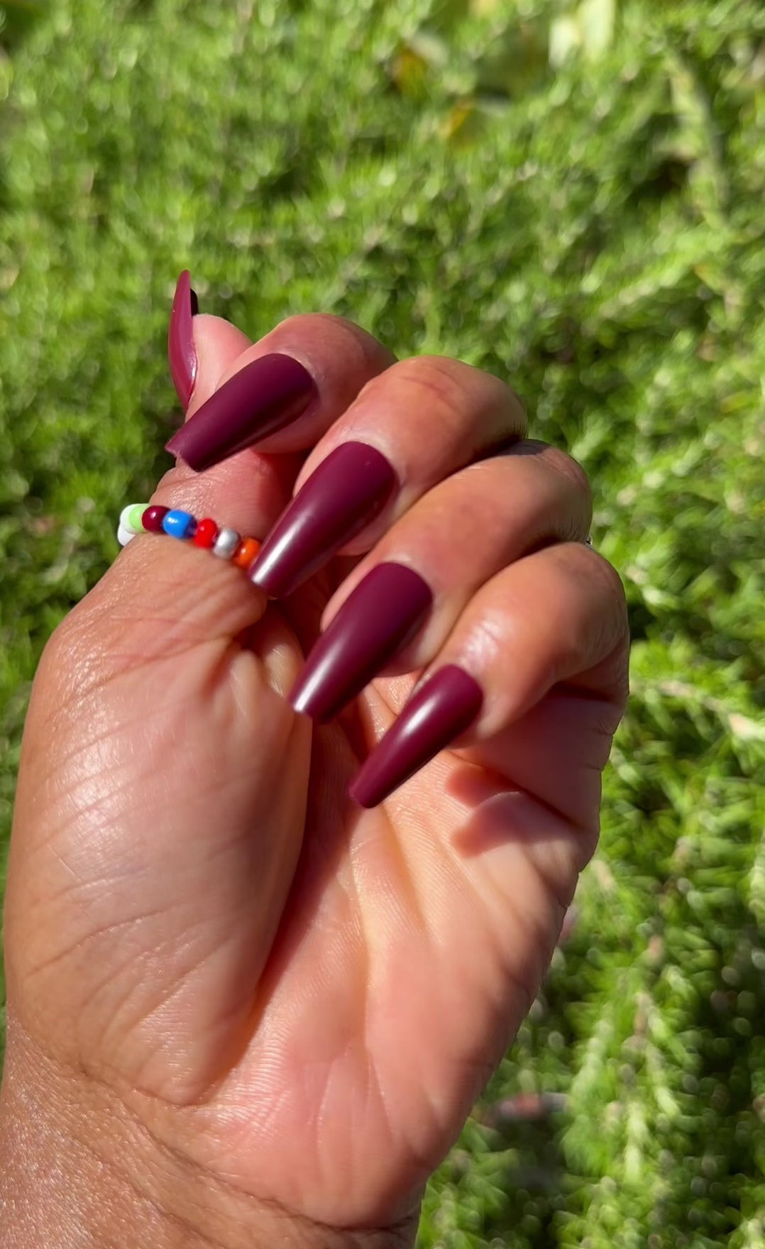 Close-up of burgundy press-on nails with colorful ring